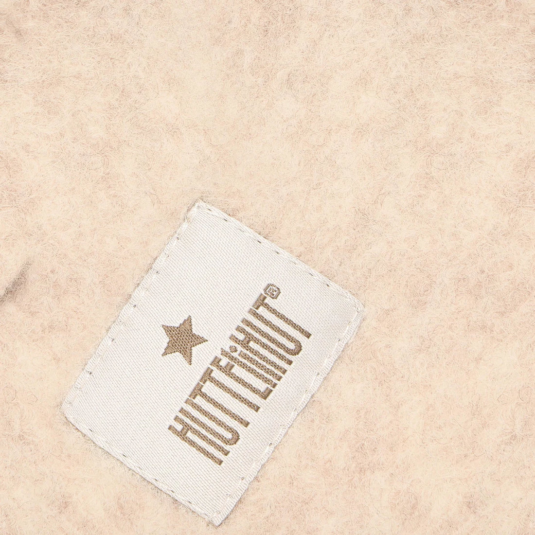 Close-up of the HUTTEliHUT label and textured Sand melange wool fabric
