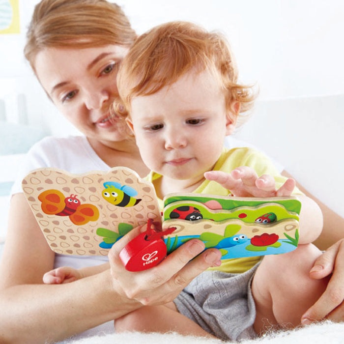 Hape Baby's Bug Book wooden infant toy; colorful bug pages, baby turning a page under caregiver's guidance.