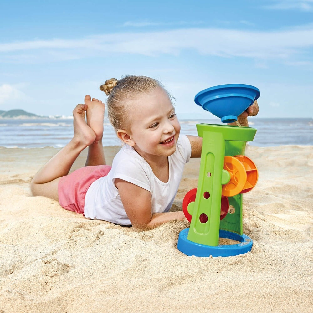 Hape Doule Sand and Water Wheel on the beach; green tower with blue funnel and orange wheels.