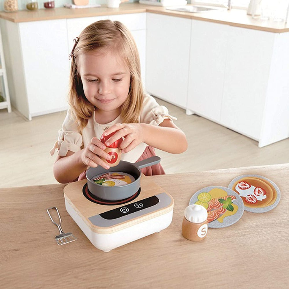 Hape Fun Fan Fryer toy set with gray pan on wooden stove; toddler cooks pretend food.