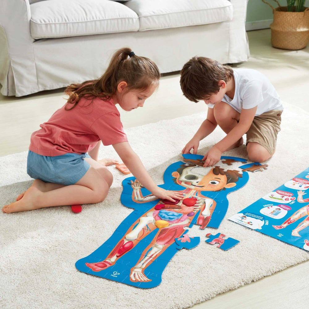 Hape Human Body Puzzle; two kids assemble a colorful anatomical puzzle on a blue silhouette.