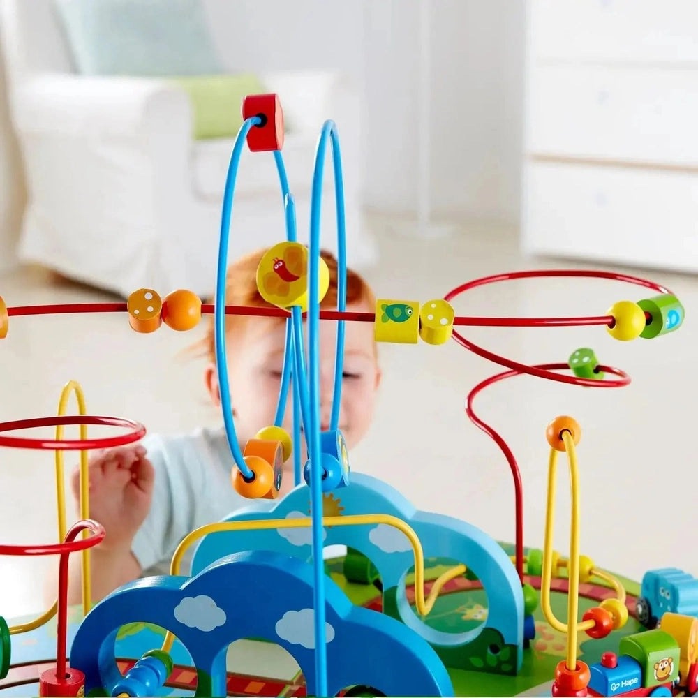 Hape Jungle Adventure Railway Table with bright blue bead-maze rails; toddler pushes beads along colorful tracks.