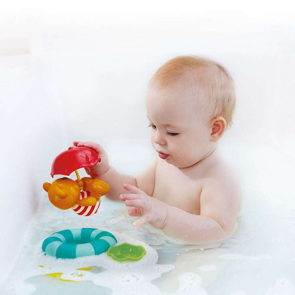 Hape Rainy Day Catching Set with bright red umbrella; baby playfully grasps floating orange animals in a bath.