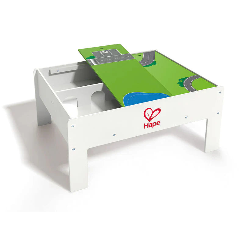 Hape Reversible Train & Storage Table, white frame and green top with road map and tracks, under-table storage visible.