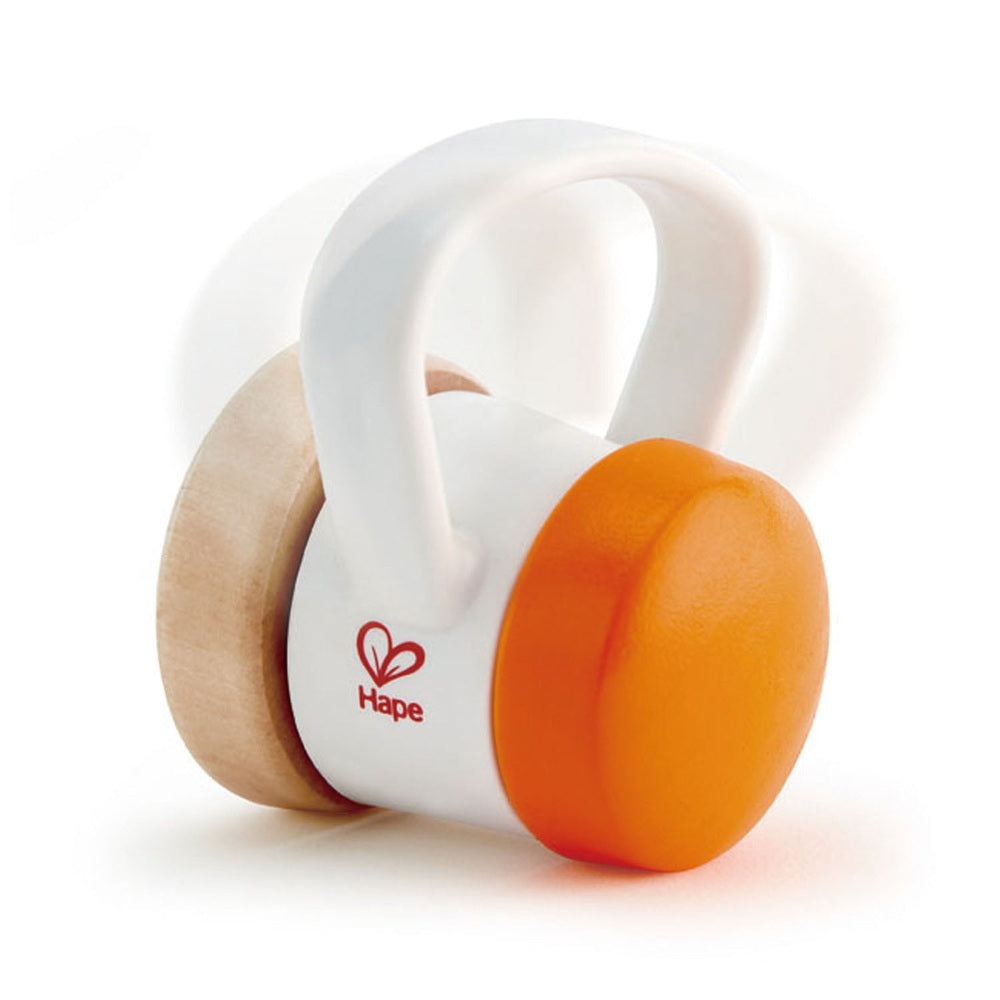 Hape Roller Rattle white body with orange wheel rolling on natural wood base.