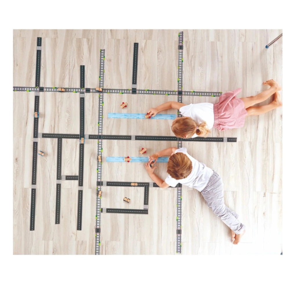Hape Tape & Roll Train; two kids lay black tape tracks on a light floor, adding blue tape accents.