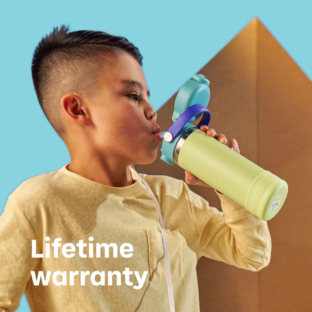 Hydro Flask Kids 18 oz Wide Mouth Bottle With Covered Straw Cap And Boot – Lifetime warranty – Child drinking from a reusable water bottle against a colorful backdrop.
