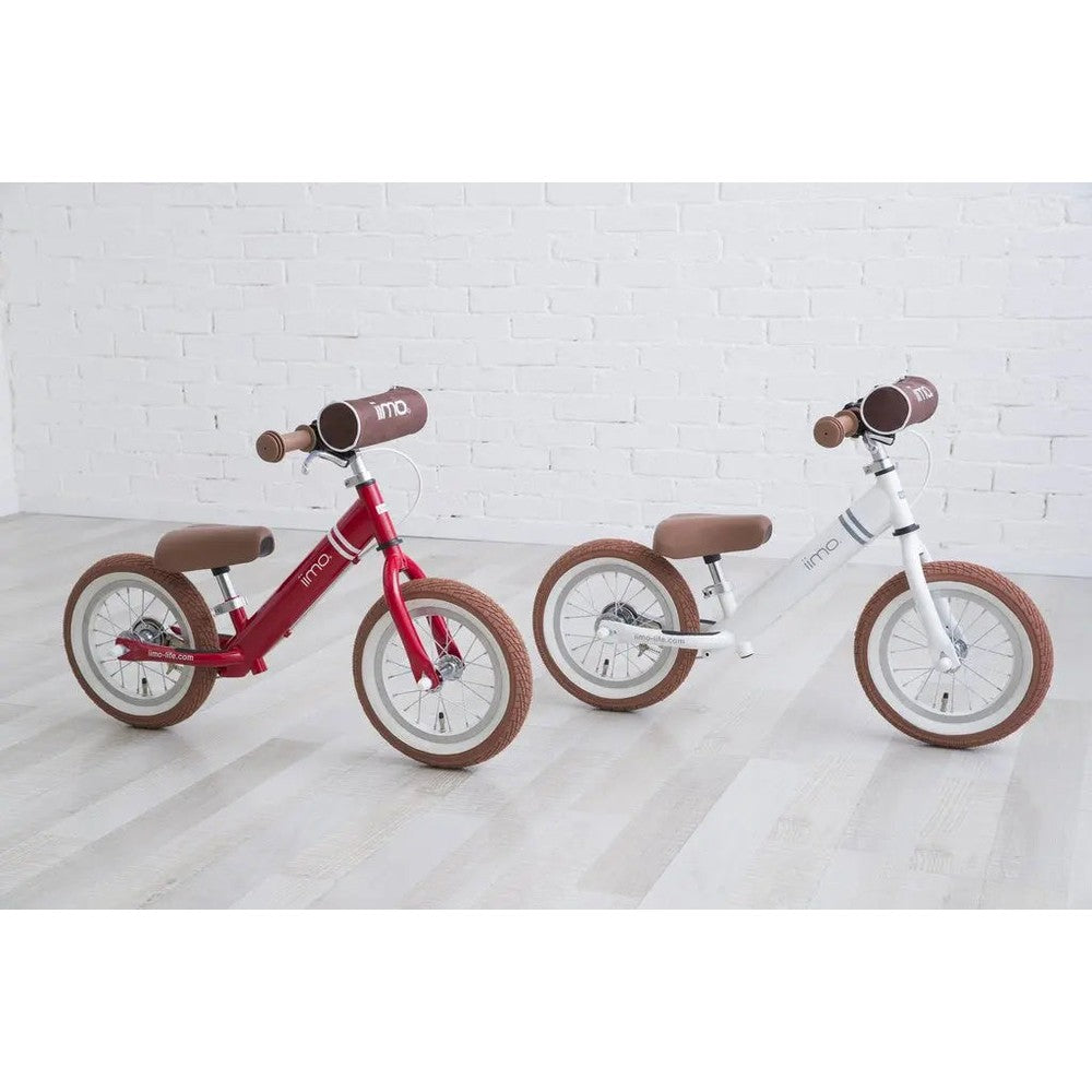 Iimo Balance Bike pair set against a white wall; red and white frames with brown saddles and grips.