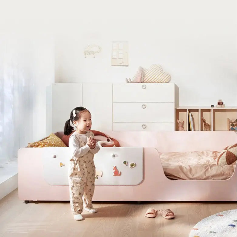 ILOOM Eddi Kids Low Bed 1100W in pink and white; a toddler stands beside the low bed with decorative decals in a bright nursery.