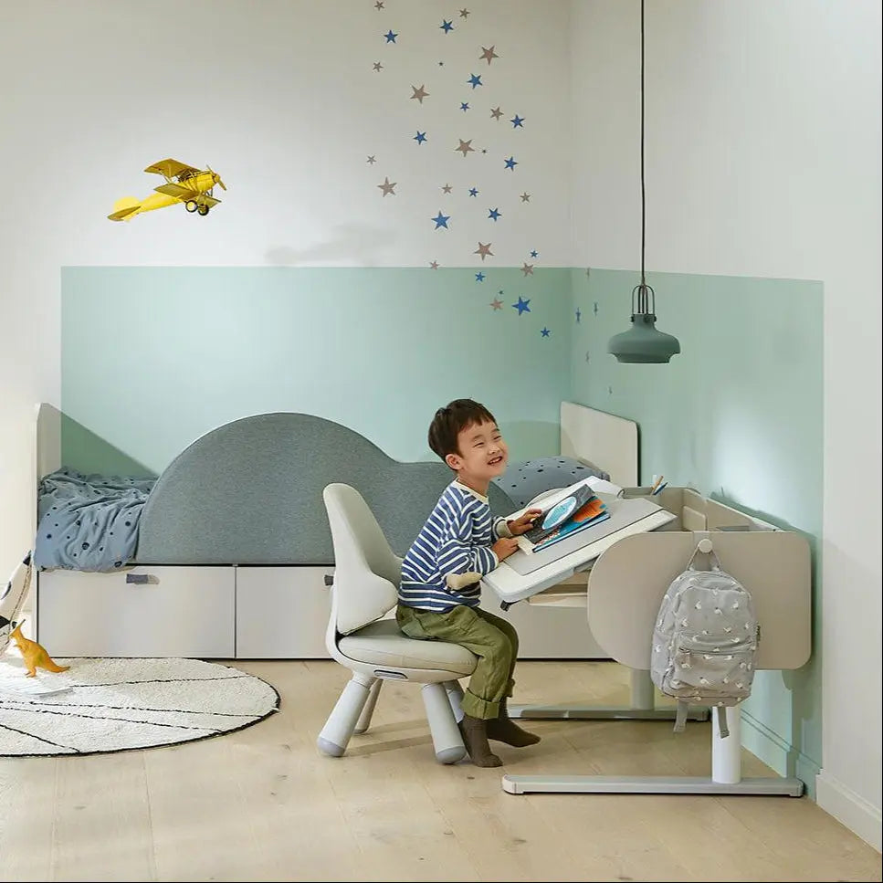 Iloom Jerome Motion Desk, white adjustable kids desk with curved panel; child sits and writes at the height-adjustable surface.
