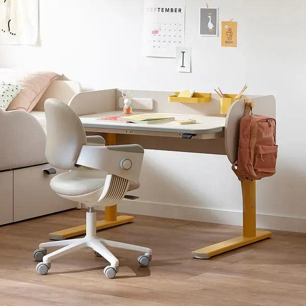Iloom Jerome Motion Desk with white top and yellow frame; a backpack hangs from the leg beside a white chair.