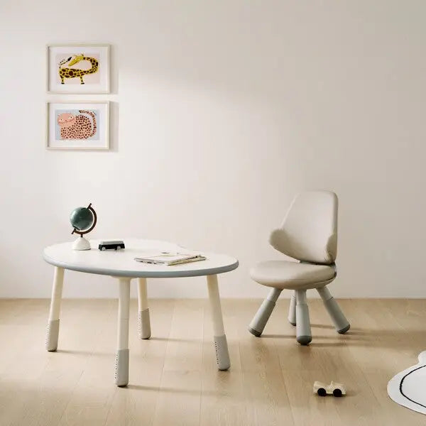 ILoom Wing Kids Chair in light gray with a rounded back and tapered legs sits beside a white round table.