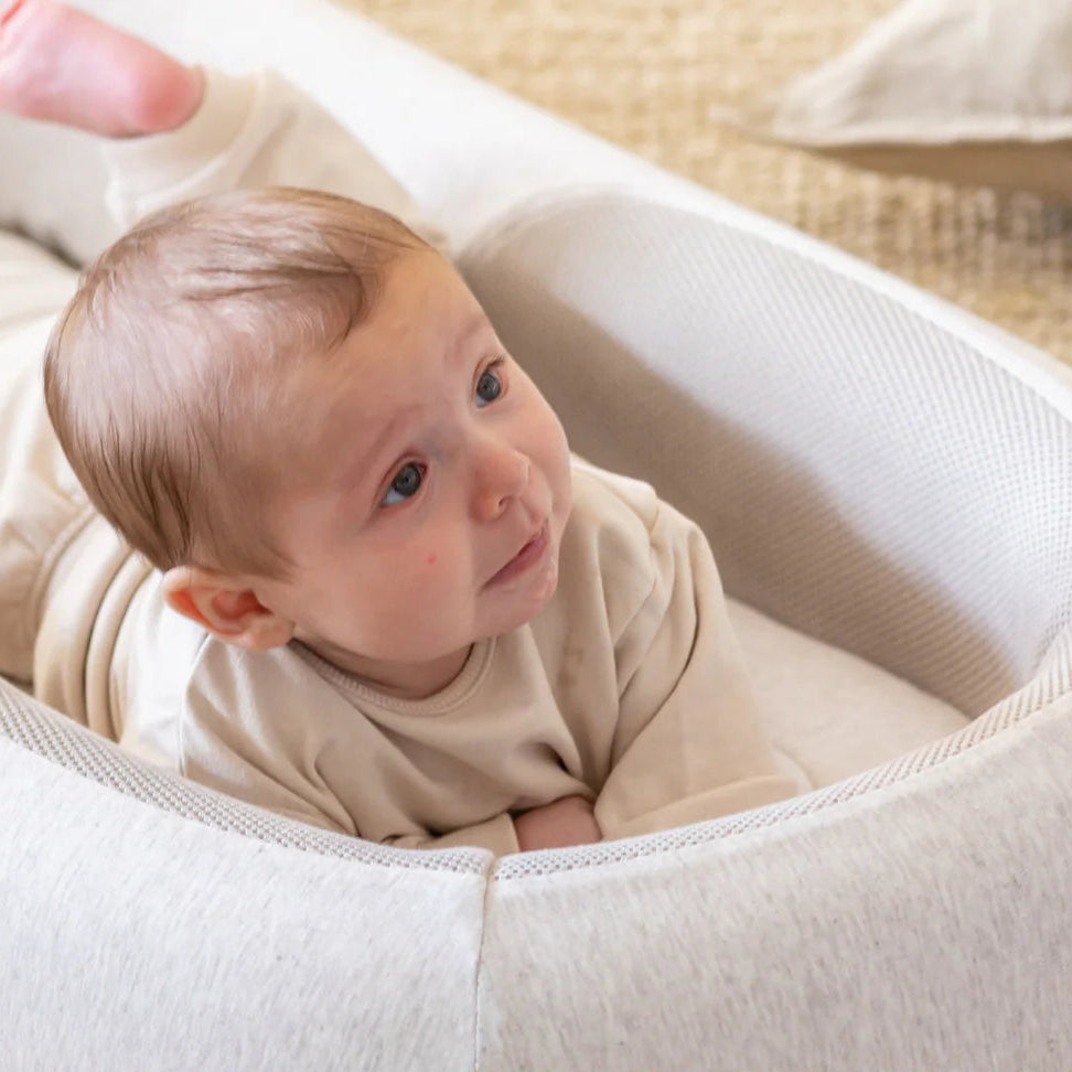 Baby lying in a white baby nest on a beige carpet