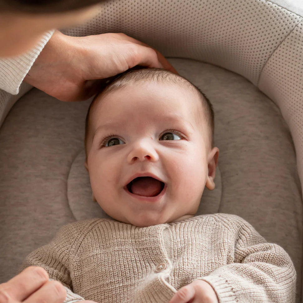 Baby in a crib with a smiling expression, being held by an adult.