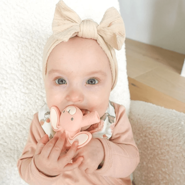 Itzy Ritzy Baby Molar Teether pink bunny design held by a smiling baby