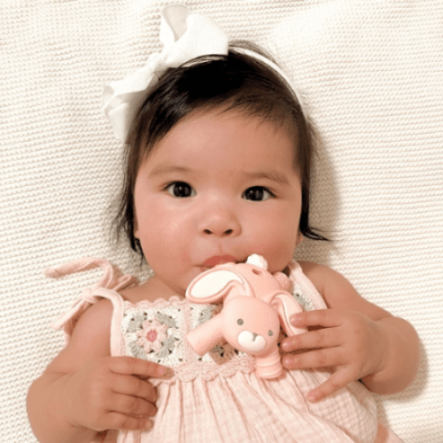 Itzy Ritzy baby molar teether pink with bunny motif, held by a smiling baby