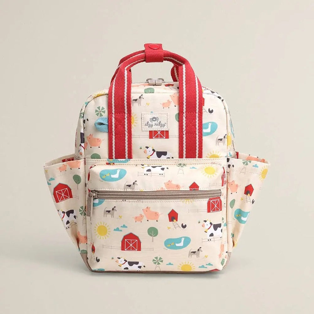 Itzy Ritzy Backpack in pastel farm print with red straps, featuring a front zip pocket and side pockets.
