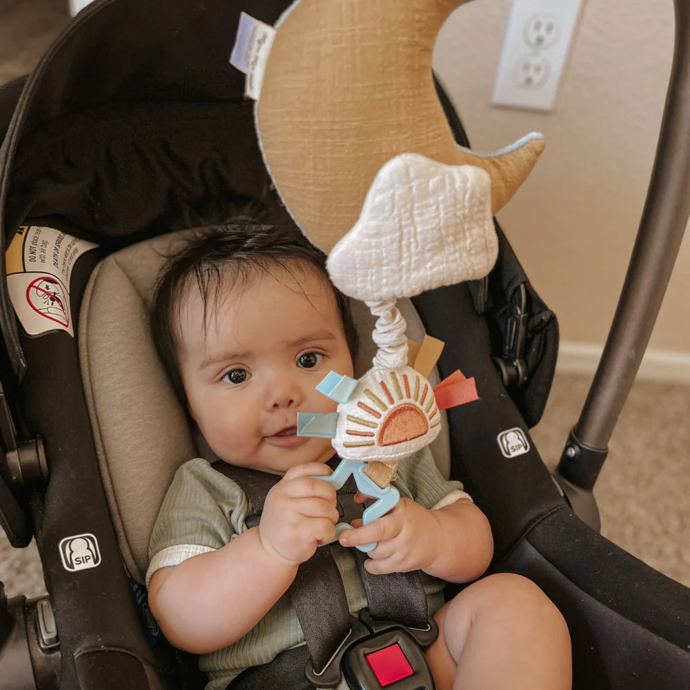 Itzy Ritzy Bitzy Notes Moon and Sun musical pull-down toy held by baby in a car seat