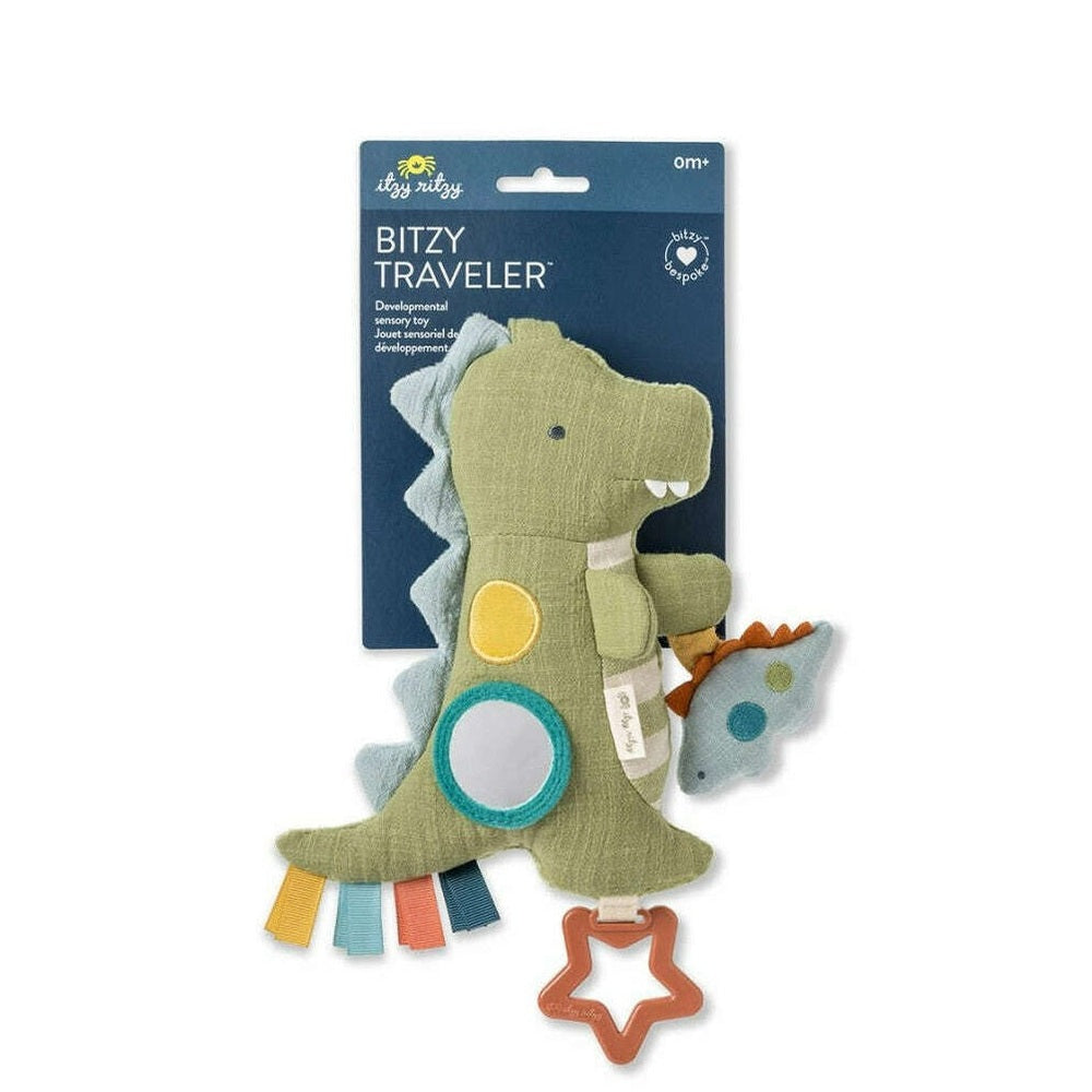 Itzy Ritzy Bitzy Traveler dinosaur plush toy, green with teal accents, ribbon tags, and star teether
