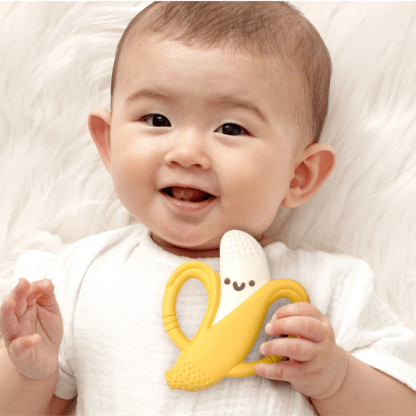 Itzy Ritzy Chew Crew teething toy, yellow with white textured tip, held by smiling baby.