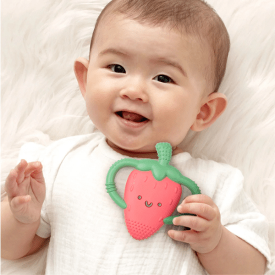 Itzy Ritzy Chew Crew strawberry teether, pink with green stem, held by a smiling baby