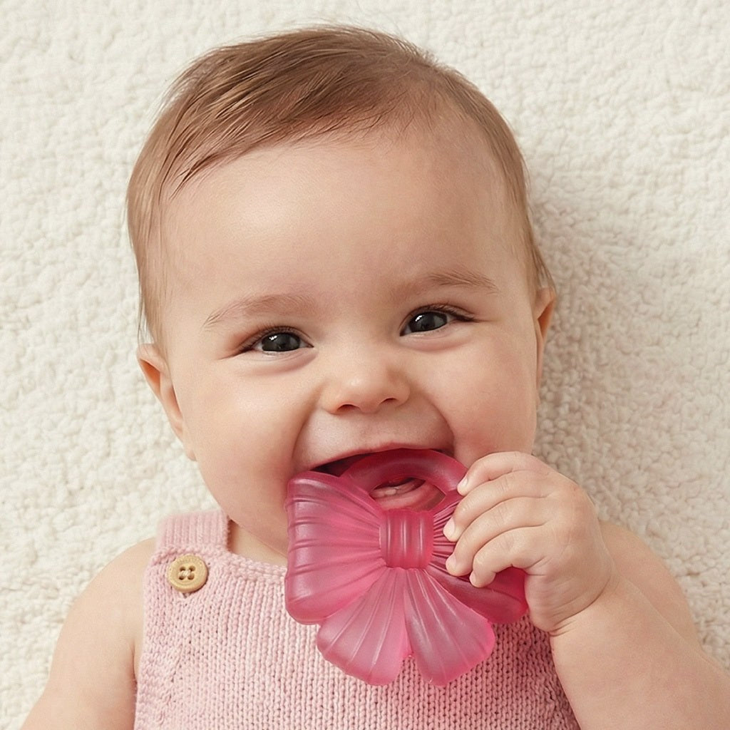 Baby holding a deep pink Coquette bow-shaped Cutie Cooler teether