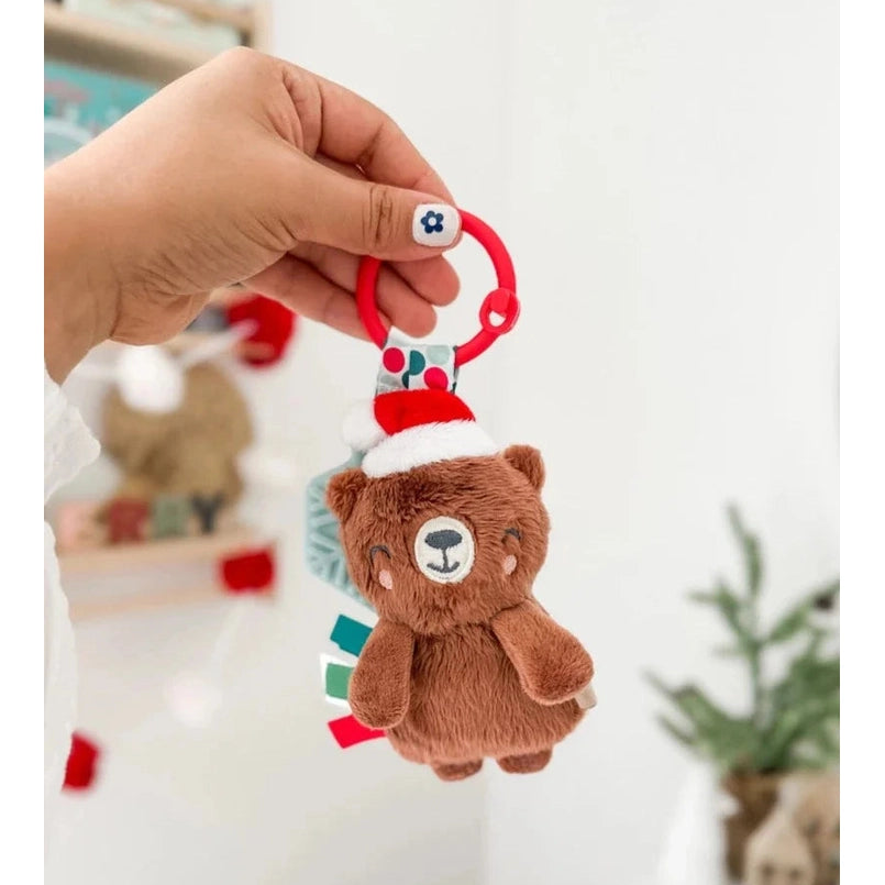 Itzy Ritzy Holiday Itzy Pal plush teether: brown bear on a red ring, Santa hat, with colorful ribbon tabs.