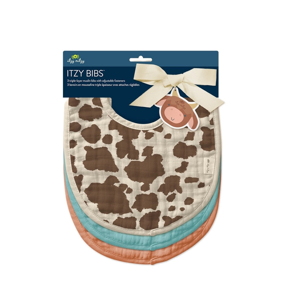 Itzy Ritzy Itzy Bibs 3-pack cow-print bibs with beige trim, layered pastel bibs underneath.
