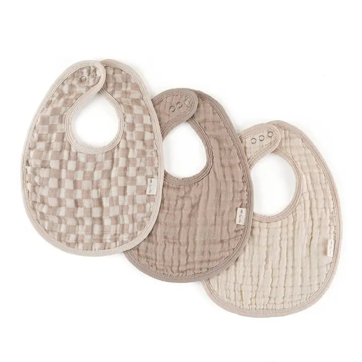 Itzy Ritzy Itzy Bibs: set of 3 beige quilted bibs with snap closures, laid flat for mealtime.