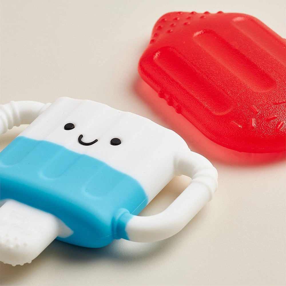 Itzy Ritzy Itzy Cool teething toy in blue and white with a smiling face; red accessory in background.