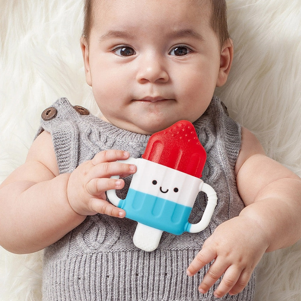 Itzy Ritzy Itzy Cool teething popsicle toy, red top with blue-white body, held by baby.