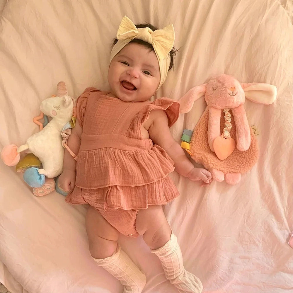 Itzy Ritzy Itzy Friends Link & Love activity plush; baby in pink ruffle romper with cream headband beside two plush bunnies