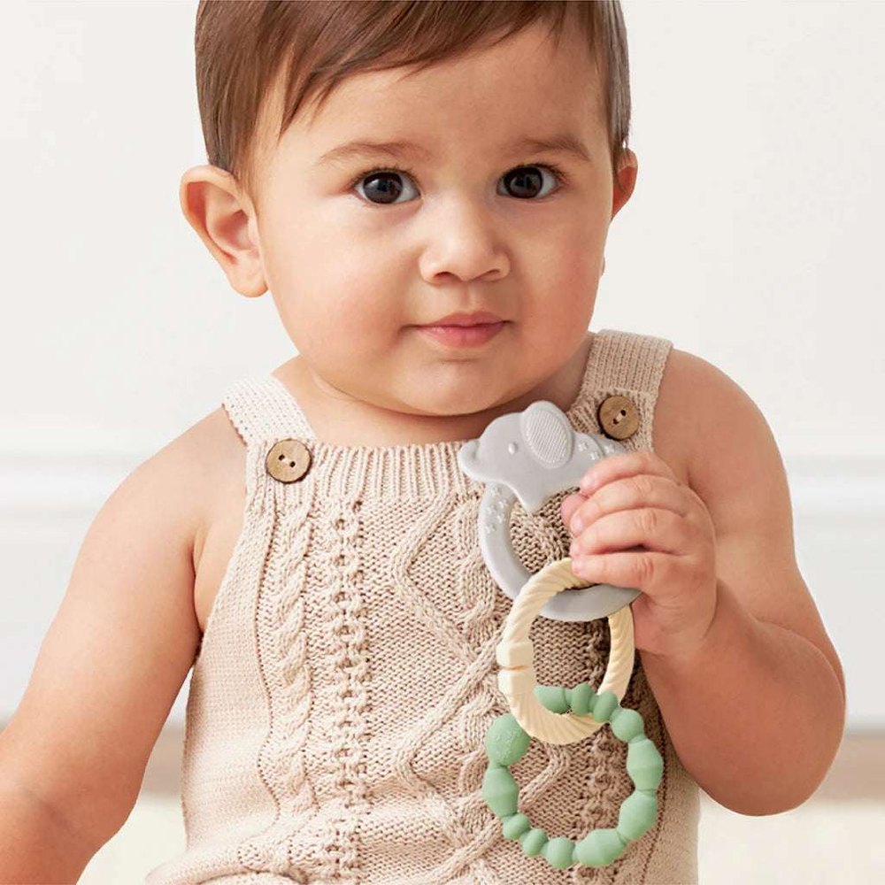 Itzy Ritzy Itzy Loops teething toy with gray elephant and mint beads, held by a baby in a beige knit romper