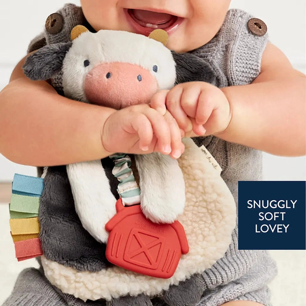 Itzy Ritzy Lovey plush and teether toy; soft cow lovey with multicolor ribbon teether and red silicone tag