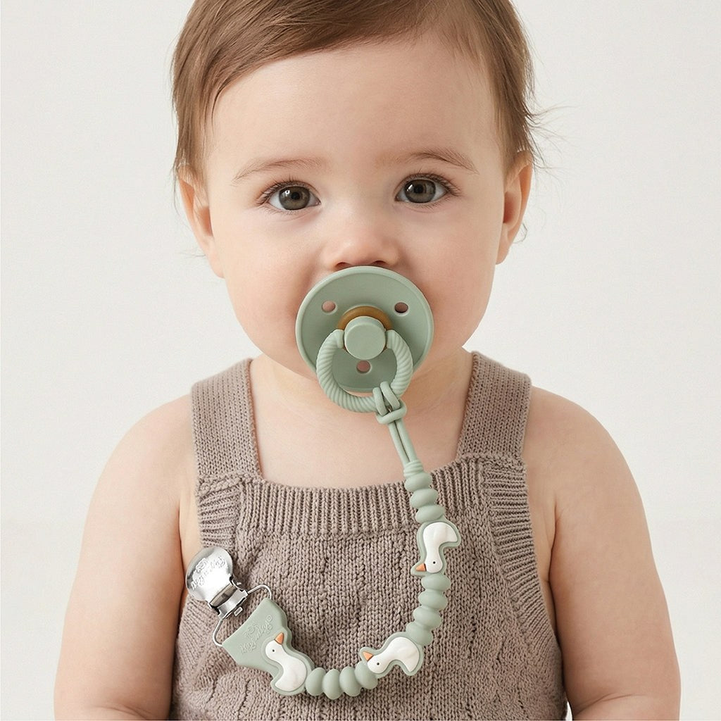Baby wearing the Goose Paci Strap Plus clipped to clothing and attached to a pacifier