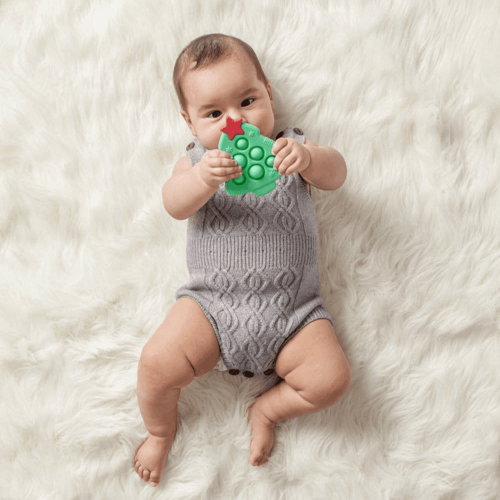 Itzy Ritzy Itzy Pop silicone toy, green with red star, held by baby on white fluffy background