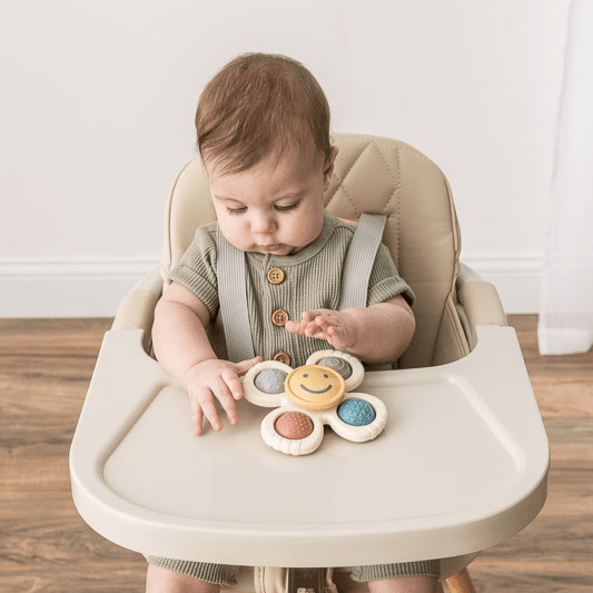 Itzy Ritzy Itzy Pop & Whirl baby toy on a high chair tray with a smiley flower and colorful discs