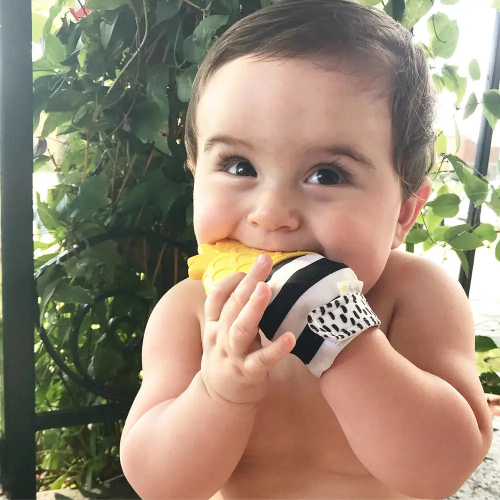 Itzy Ritzy Itzy Silicone Teething Mitts: baby chews the yellow pineapple-textured mitt with black-and-white stripe edge.