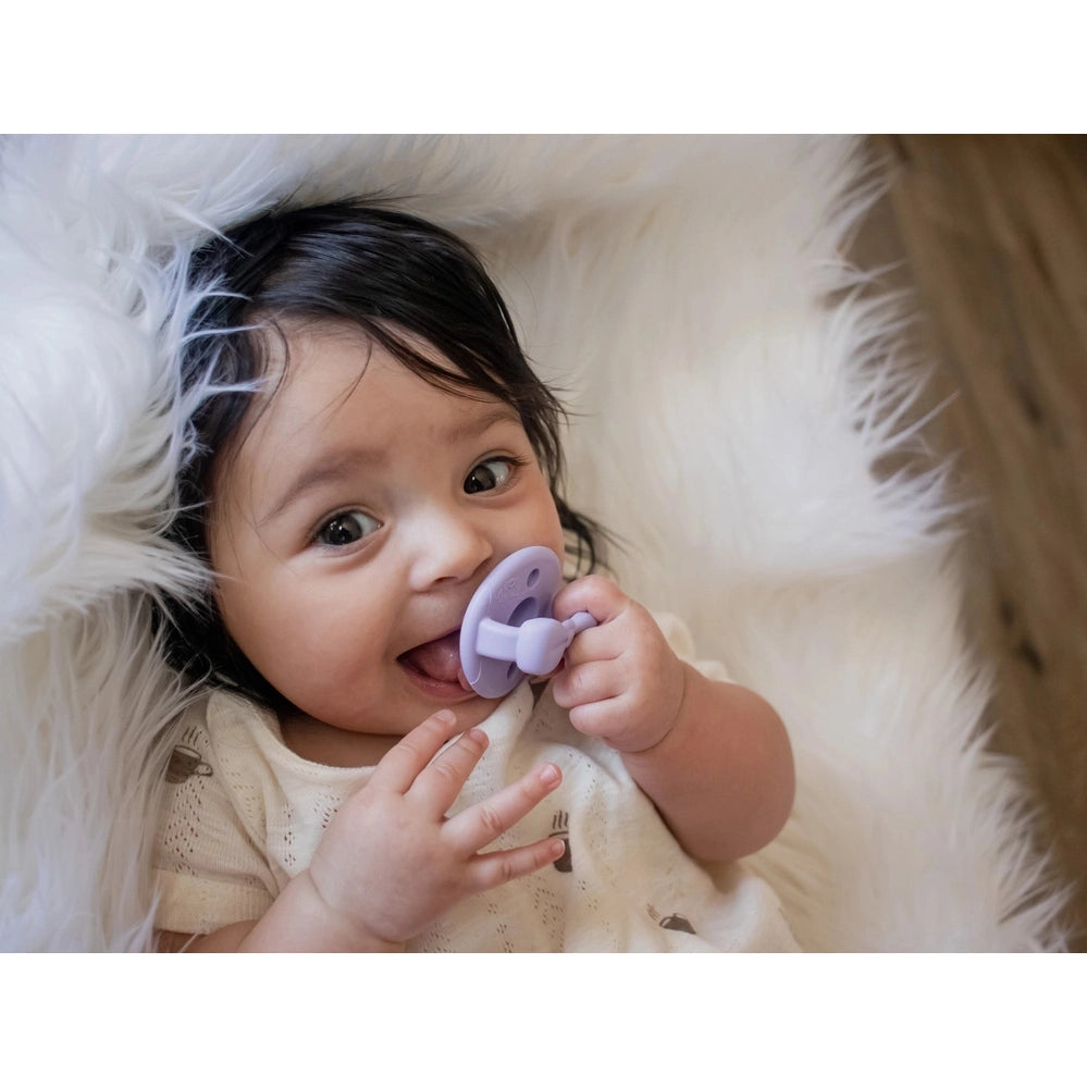 Itzy Ritzy Itzy Soother Natural Rubber Pacifier Set, lavender, for 6–18 months, as baby holds and uses pacifier.