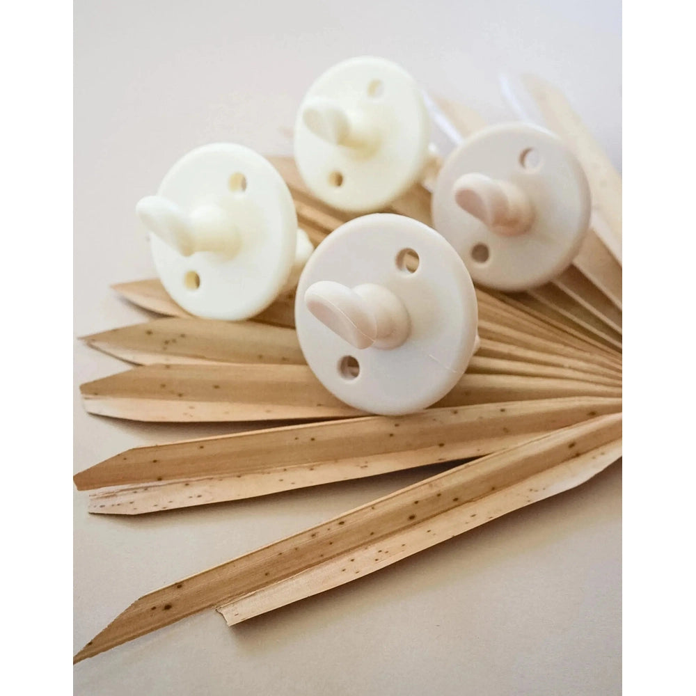 Itzy Ritzy Itzy Soother Natural Rubber Pacifier Set (0–6M); four white pacifiers sit on pale wooden leaves.