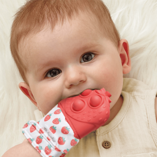 Itzy Ritzy Mitt Pop teething mitten in red silicone with strawberry-pattern fabric, baby chewing on it for soothing comfort.