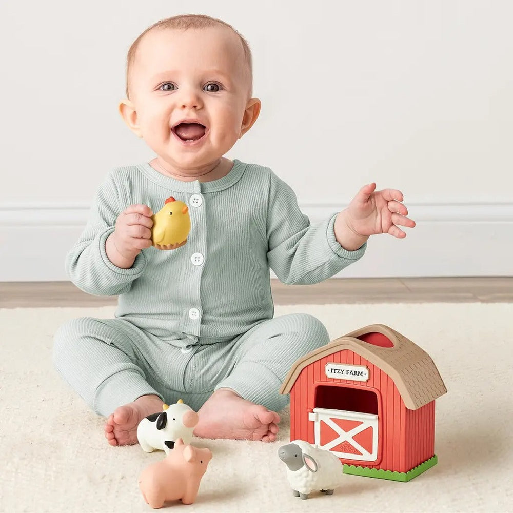 Itzy Ritzy Play Barn Spill and Fill Activity Toy: baby sits on the floor with a red barn and farm animals, holding a yellow chick.