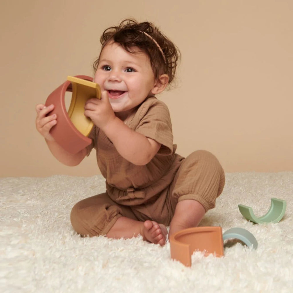 Itzy Ritzy Rainbow Stacking Toy; baby playing with pastel arch pieces on cream rug