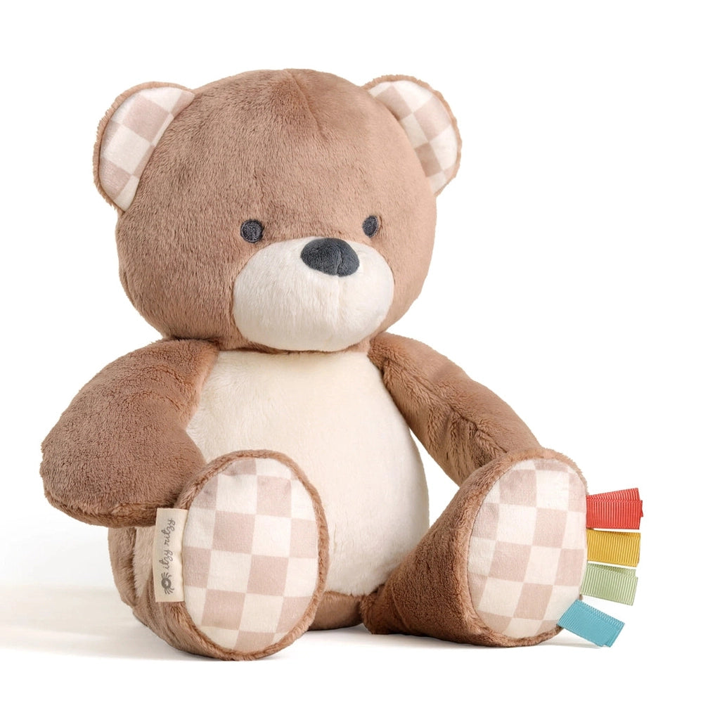 Itzy Ritzy Sweetie Snuggles Plush bear toy in brown with cream belly sits upright, checkered paws, colorful tabs.