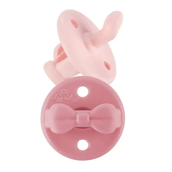 Itzy Ritzy Sweetie Soother Orthodontic Pacifier Sets (0-6M) in pink, featuring a bow-shaped guard and bunny-ear clip.