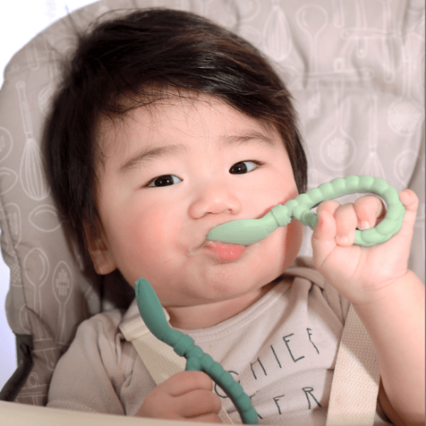 Itzy Ritzy Sweetie Spoon & Fork Set in mint silicone; baby happily grips the soft utensils during mealtime.