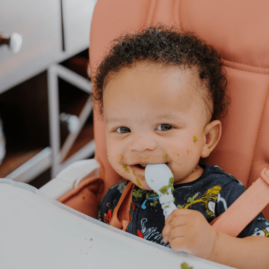 Itzy Ritzy Sweetie Spoon & Fork Set, baby feeding with spoon as green food smeared on cheeks.