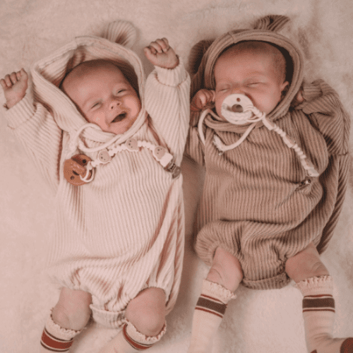 Itzy Ritzy Sweetie Strap Plus pacifier clips on two babies in beige knit sleepers, brand ITZY RITZY.