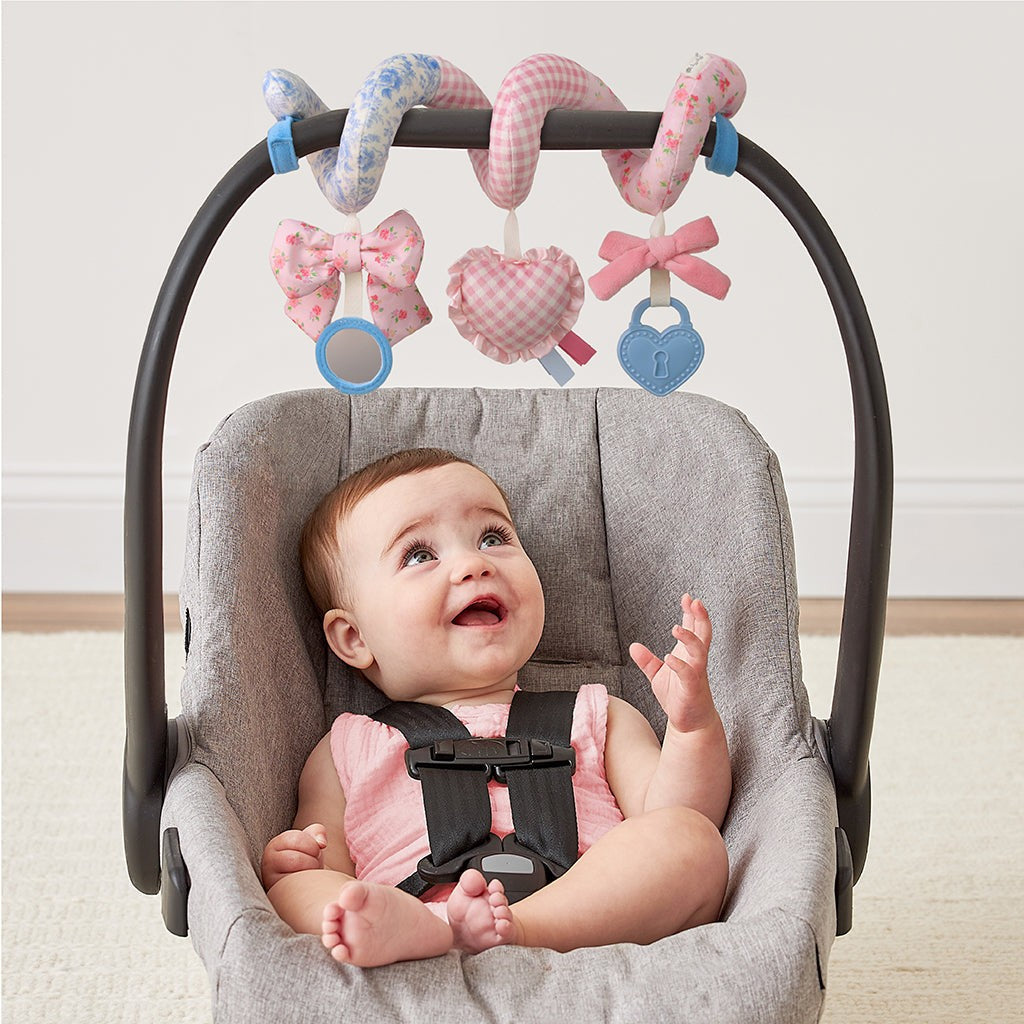 Baby reaching for the Itzy Bitzy Spiral Ribbons & Roses toy on a car seat handle