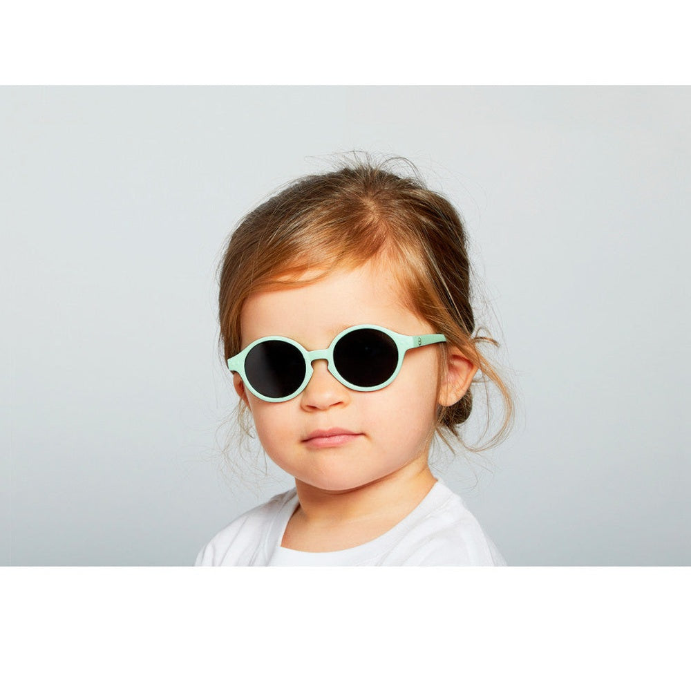 IZIPIZI Kids Sky Blue sunglasses with round mint frames worn by a young child